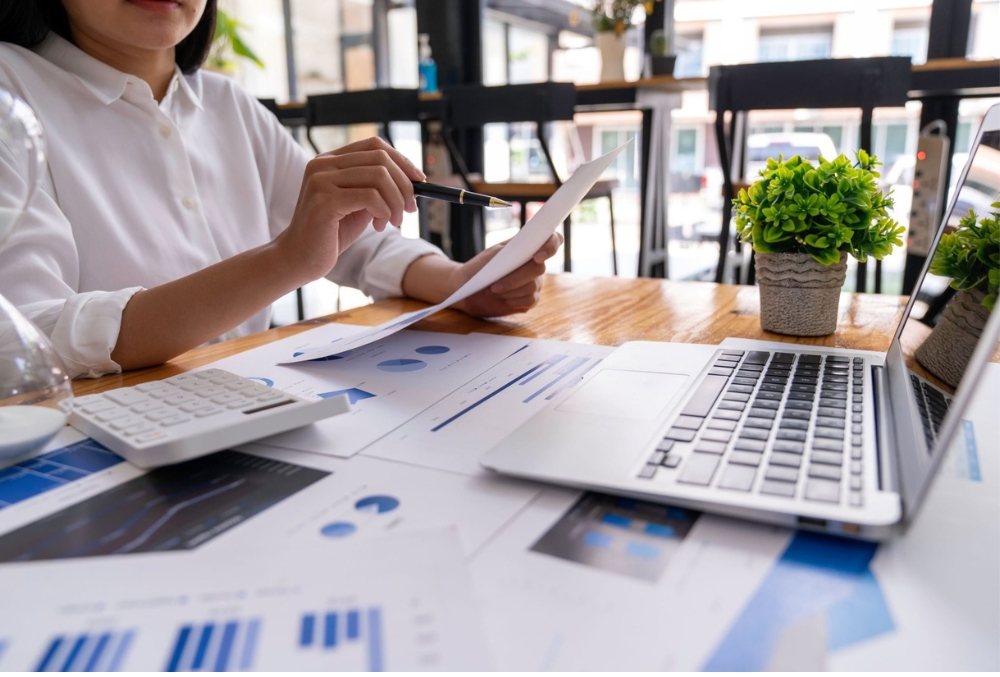 A business professional analyzing financial data on a laptop, reviewing cost reports and charts to optimize expenses and improve company profitability.
