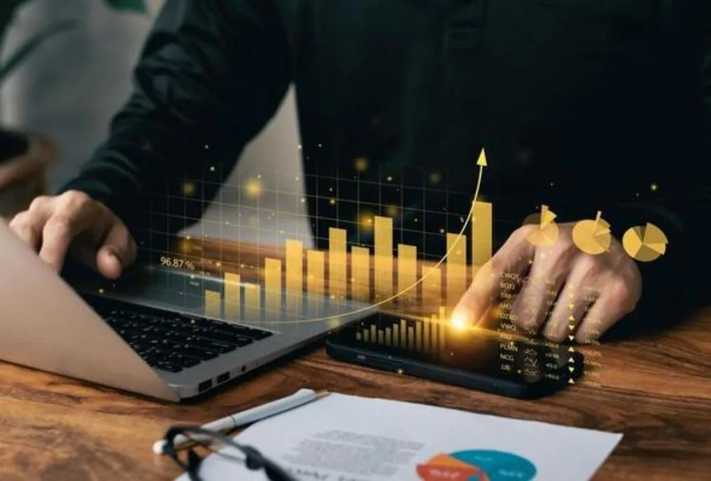A financial consultant discussing cost-saving strategies with a business owner, analyzing reports and data on a laptop to improve financial efficiency.